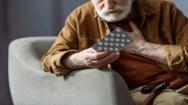 Older man holding his chest and a packet of pills